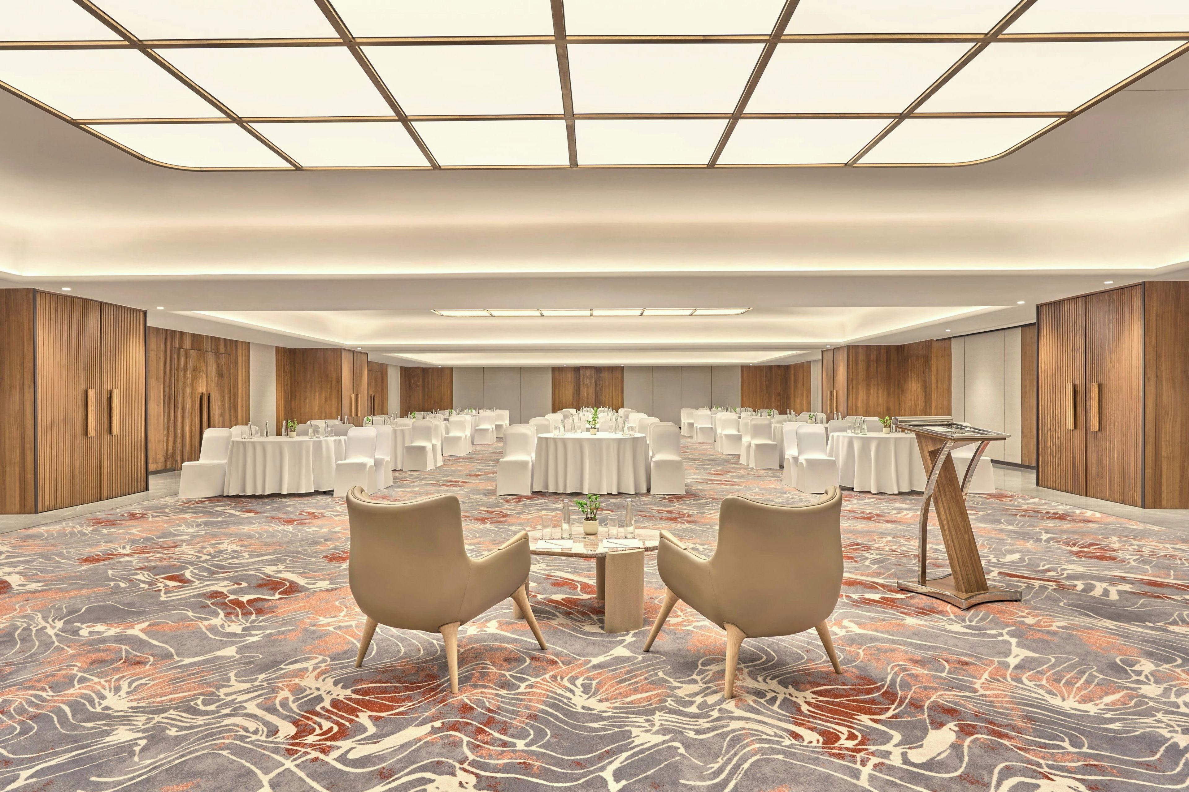 A spacious conference room with round tables, white chairs, and a patterned carpet.