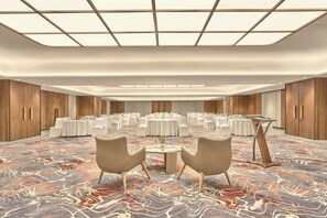 Una amplia sala de conferencias con mesas redondas, sillas blancas y una alfombra estampada.