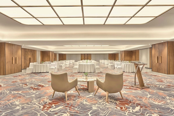 A spacious conference room with round tables, white chairs, and a patterned carpet.