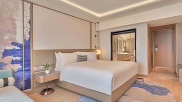 Habitación de hotel moderna con una cama grande, una mesita de noche y un baño visible a través de una puerta abierta.