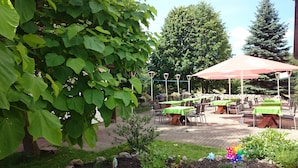 Een terras buiten met tafels en stoelen, omringd door groen en bomen.