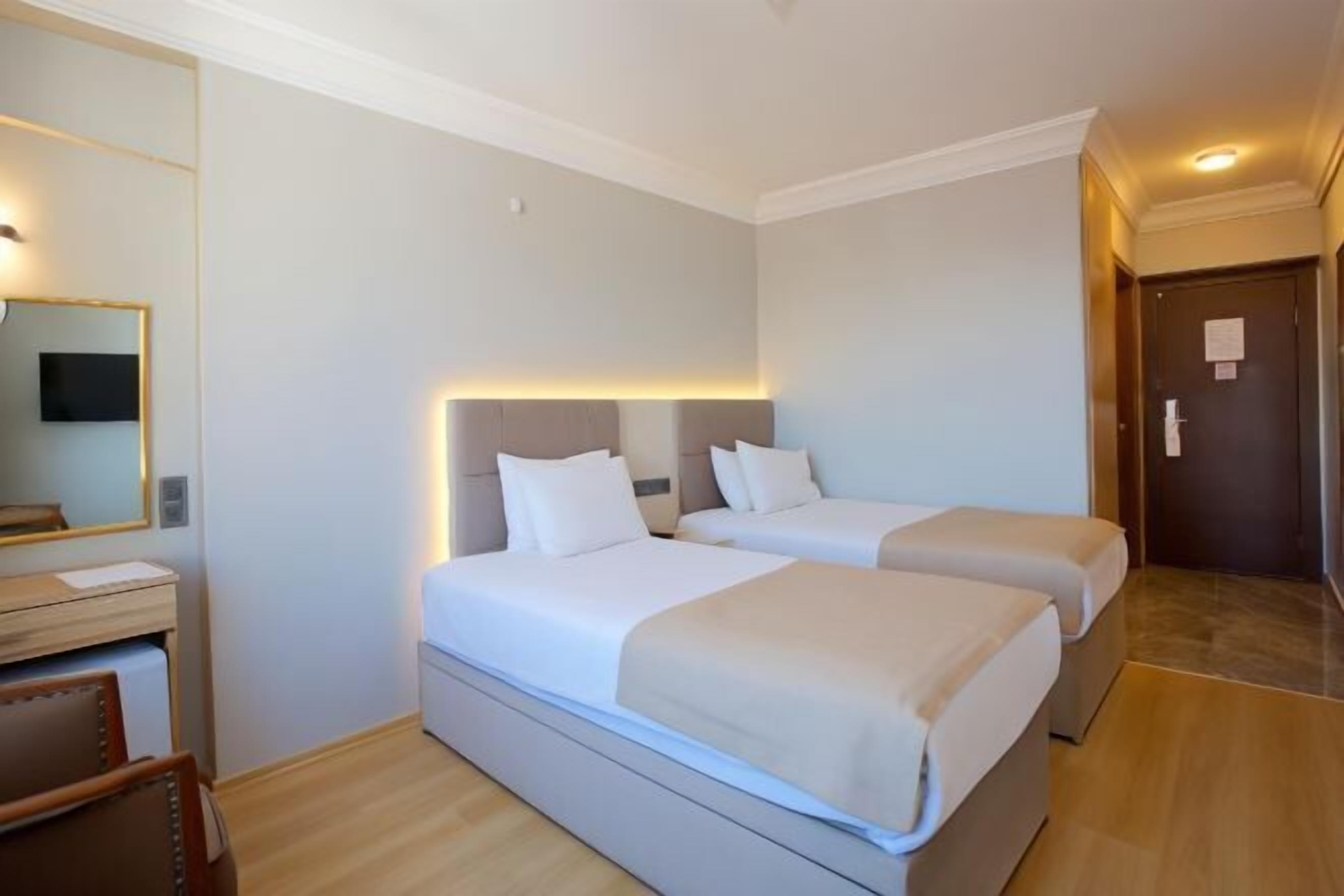Quarto de hotel com duas camas, uma escrivaninha e um espelho.