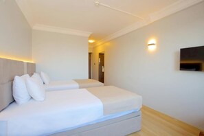 Habitación de hotel con dos camas, un televisor de pantalla plana montado en la pared y suelo de madera.