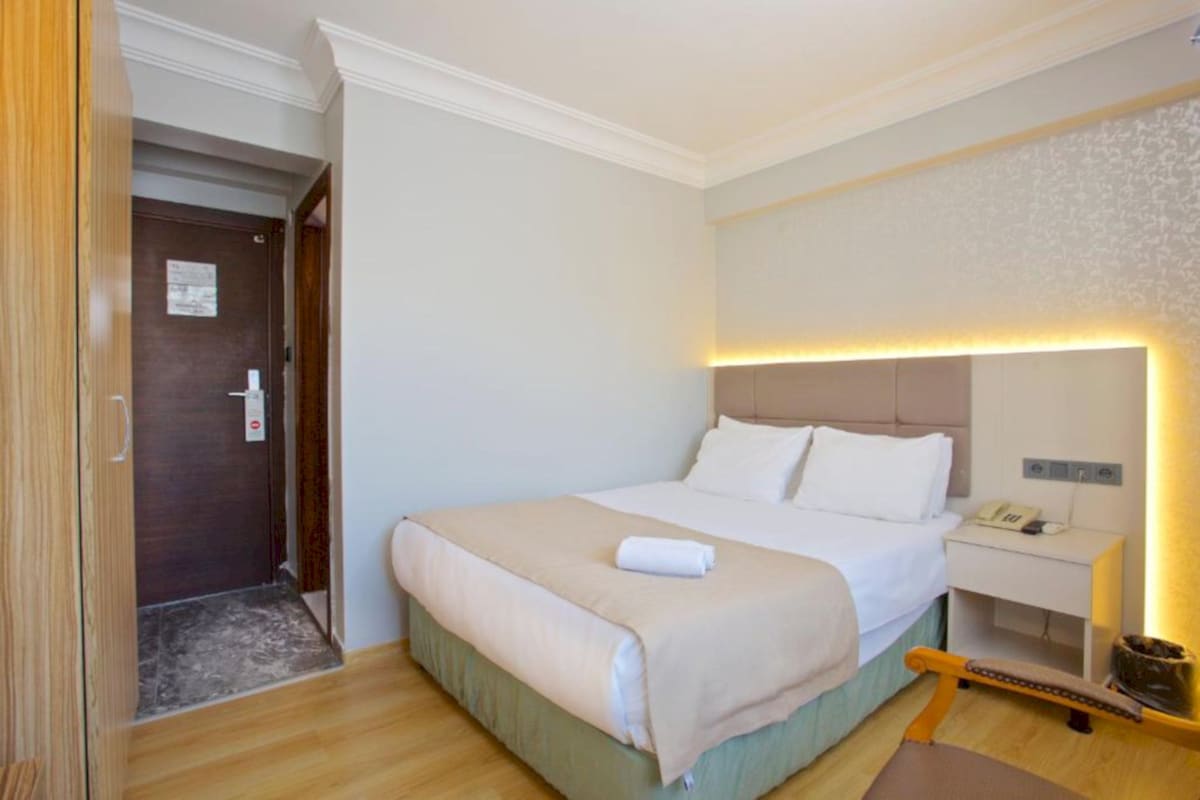 Una habitación de hotel con cama, mesita de noche y puerta.