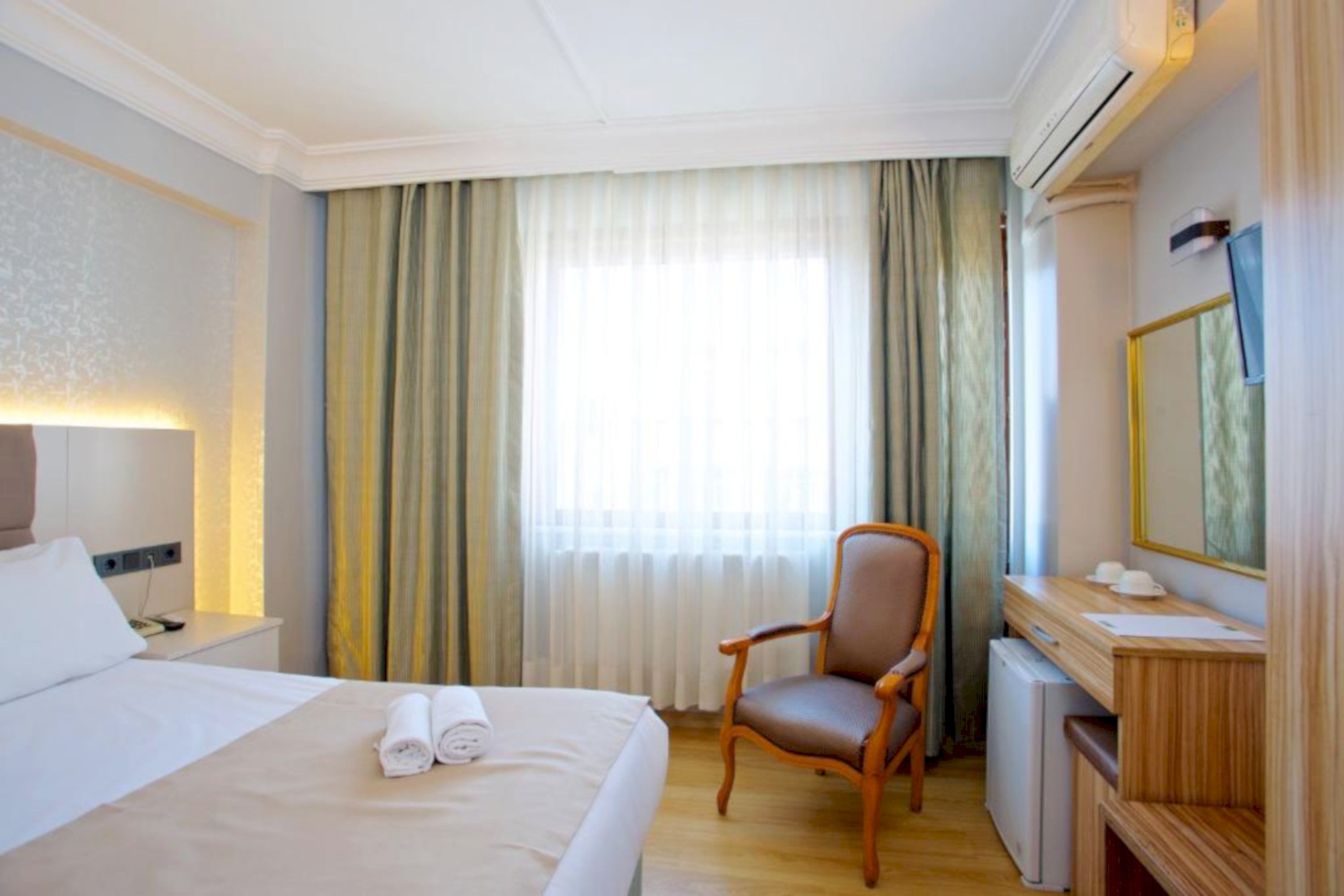 A hotel room with a bed, a chair, a desk, and a mirror.