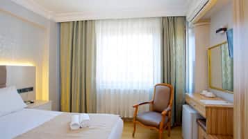 A hotel room with a bed, a chair, a desk, and a mirror.