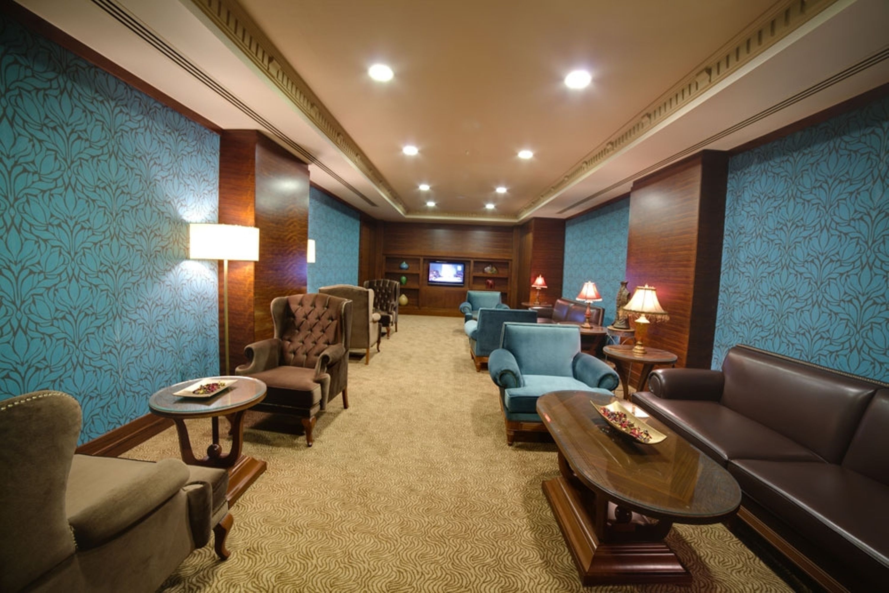 A hotel lobby with a carpeted floor, a television, and seating arrangements including a sofa and armchairs.