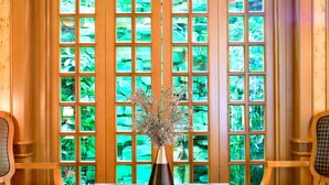 Ein Zimmer mit einer großen Holztür, die mehrere Glasscheiben aufweist, einem Tisch mit einer Vase, zwei Stühlen und einem gemusterten Teppich.
