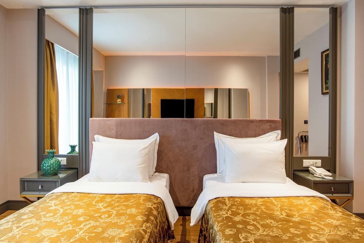 A hotel room with two beds, a large mirror, a flat-screen TV, and a wooden headboard.