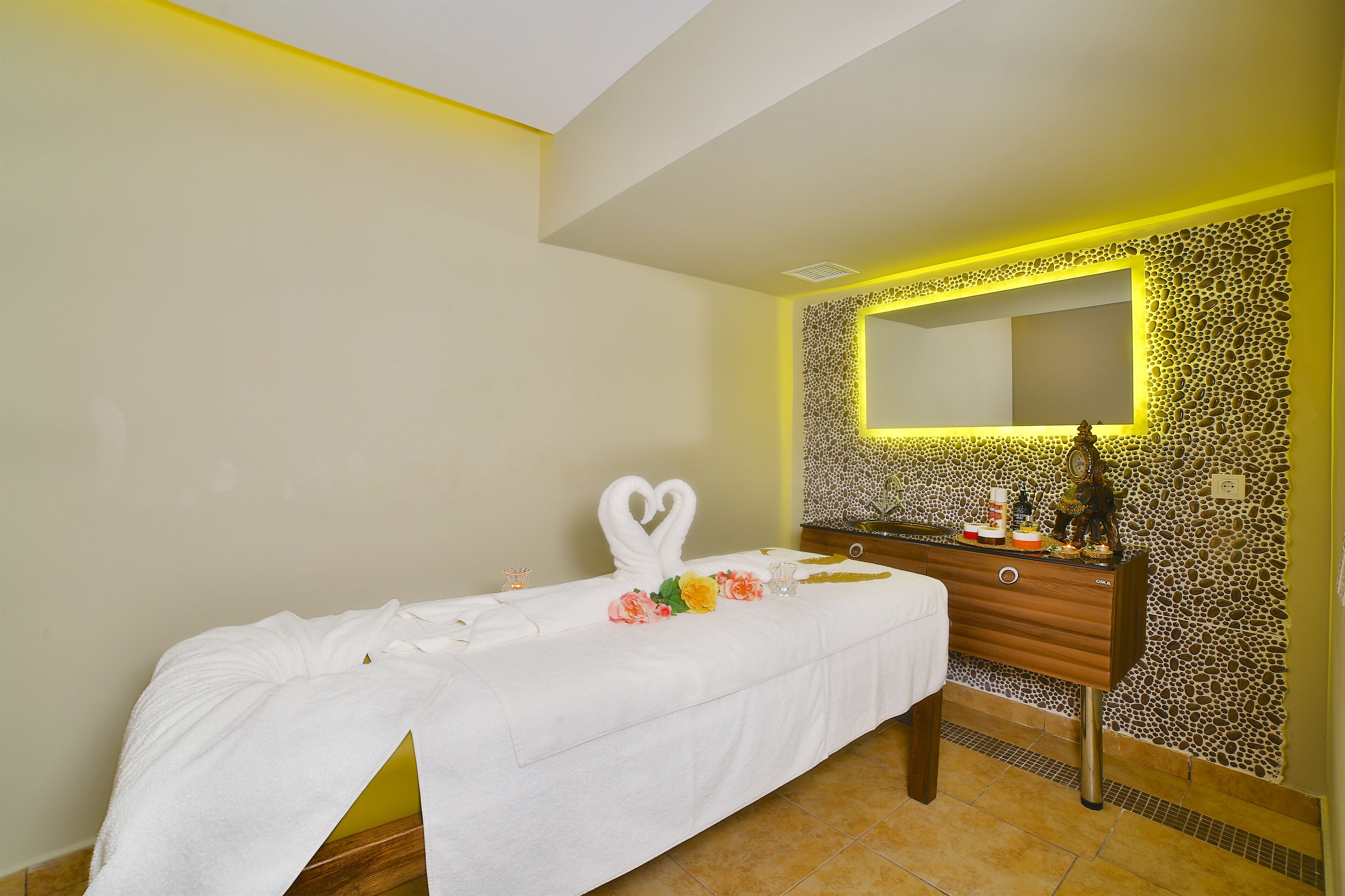 A hotel room with a bed covered in white linens, a wooden dresser with a mirror, and a decorative wall with a textured pattern.