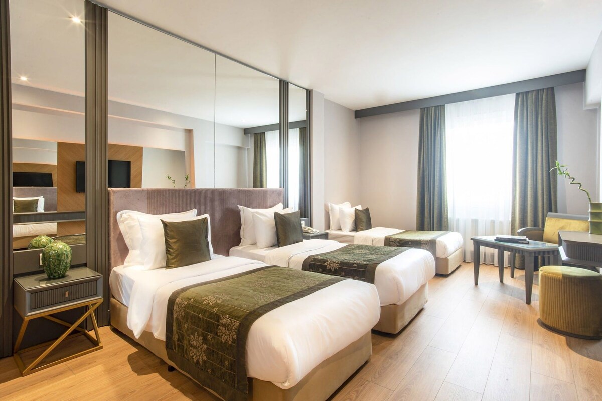 A hotel room with three beds, a desk, a chair, and a large mirror.