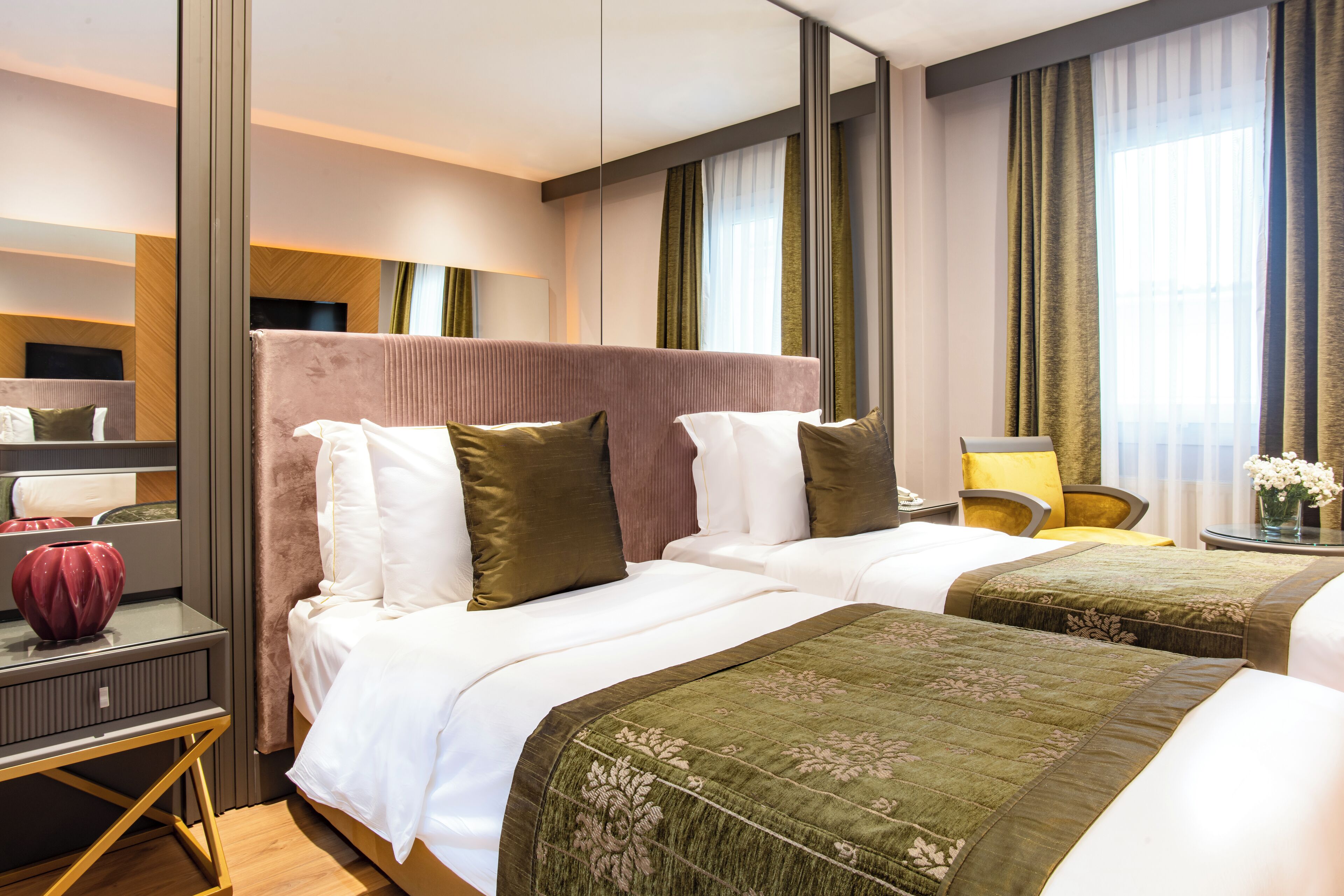 Habitación de hotel con dos camas, un escritorio, una silla, un espejo y una ventana con cortinas.