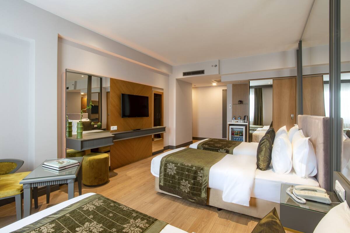 A hotel room with a bed, bedside table, and a desk with a chair. There is a television on the wall and a mirror.