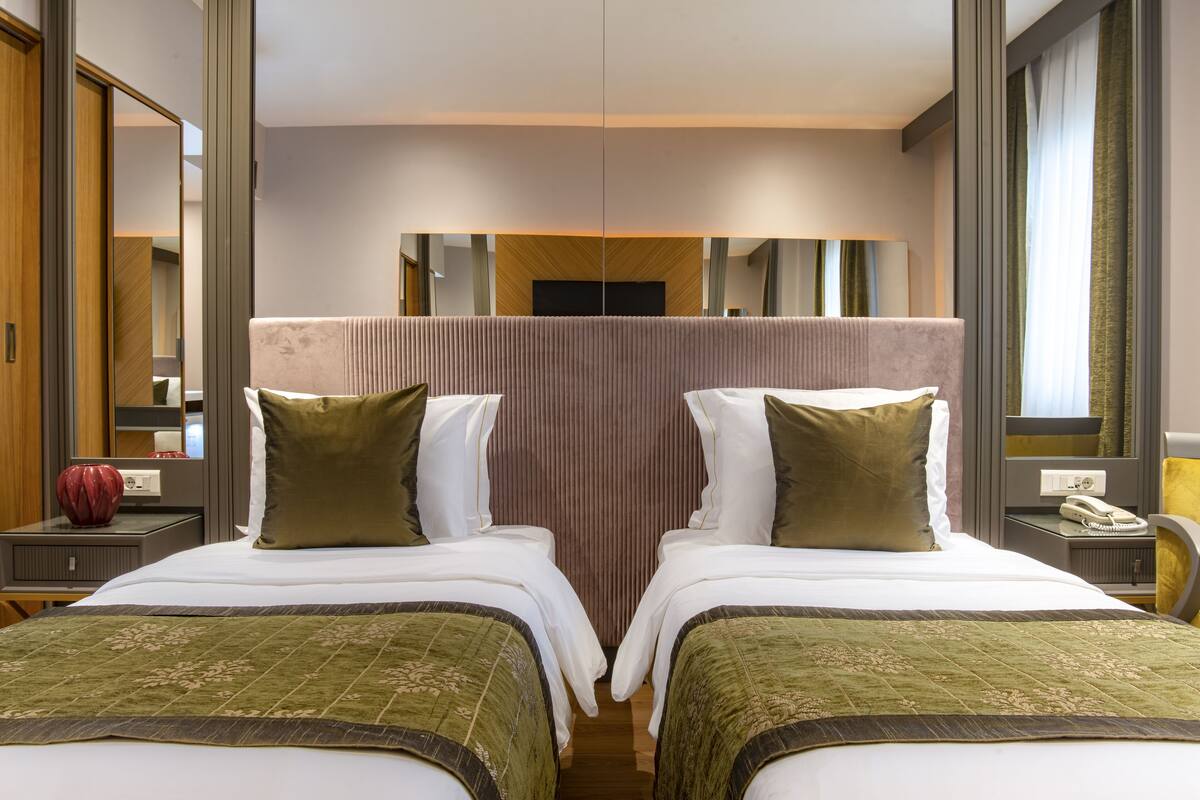 A hotel room with two beds, a large mirror, a TV, and a bedside table with a lamp and a phone.