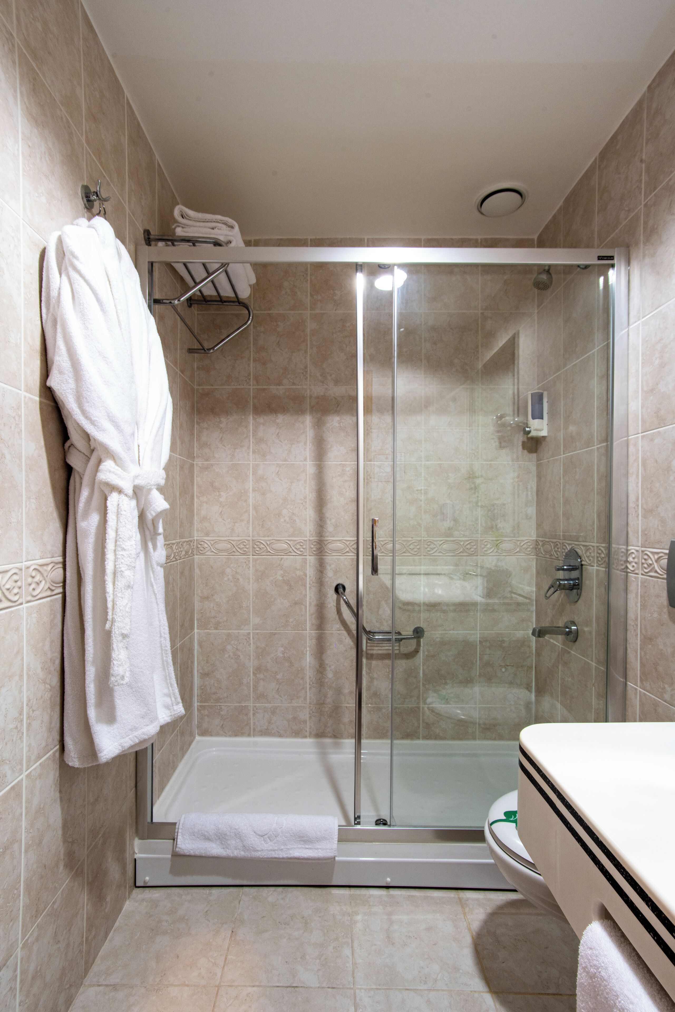 A glass-enclosed shower stall with a white towel on the floor, a glass door, and a towel rack with a white towel on the wall.