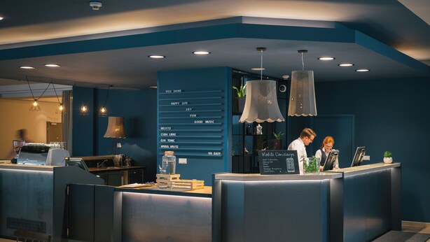 A modern coffee shop with a counter, seating area, and a menu board listing various drinks. - Vienna House Easy by Wyndham Bratislava (Bratislava)