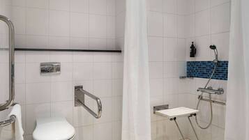 Ein Badezimmer mit Toilette, Haltegriffen, einer Dusche mit Duschbrause und einem Handtuchhalter.