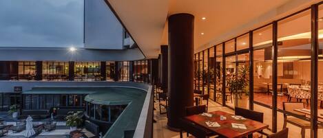 A modern hotel atrium with a pool, outdoor seating, and a view of the interior dining area.