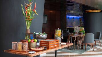 A reception area with a wooden table displaying a welcome sign, a decorative plant, a fruit bowl, and a beverage dispenser.