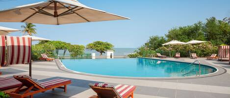 A poolside area with lounge chairs and umbrellas, a pool, and a view of the ocean.