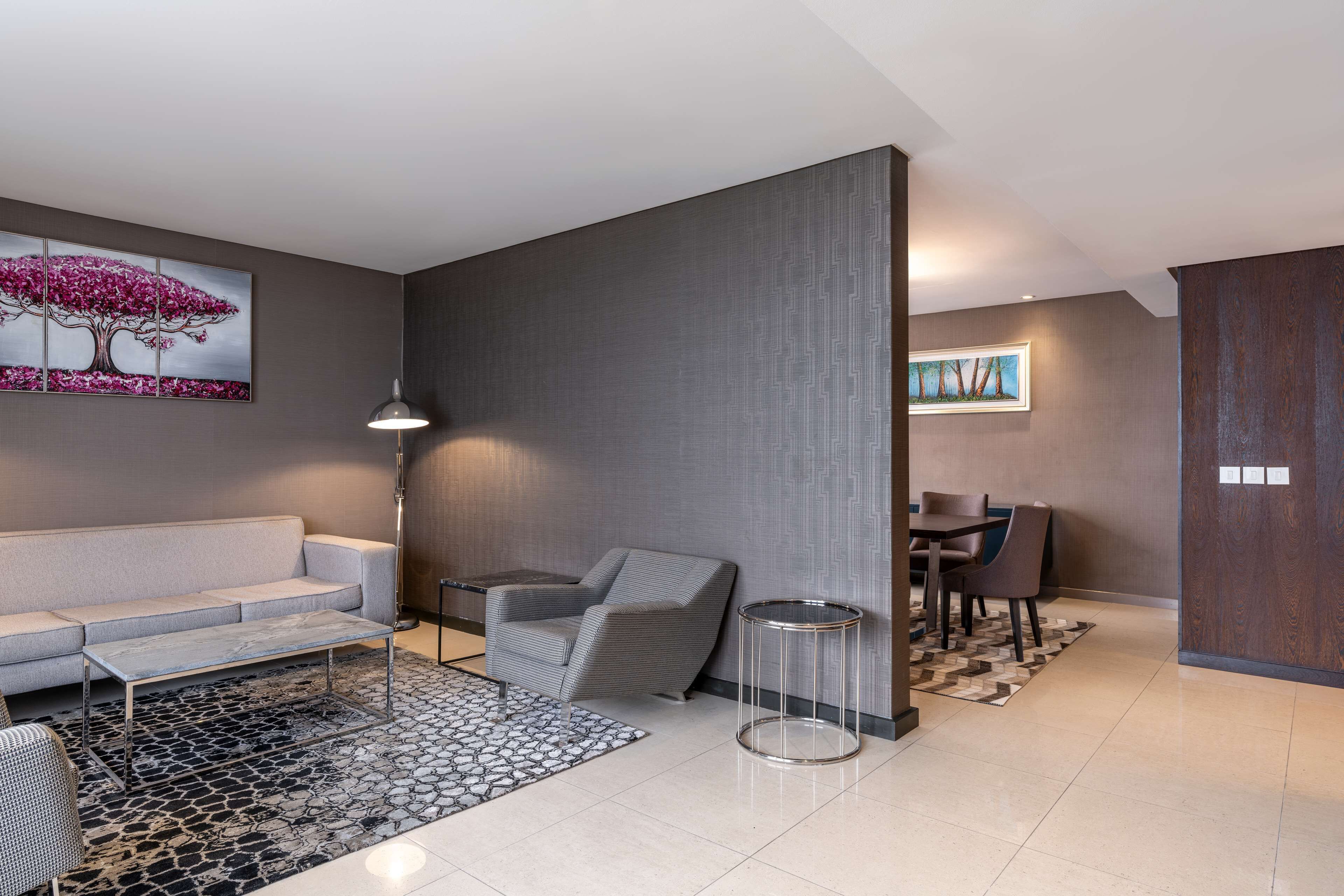 A modern living room with a sofa, armchair, coffee table, and a dining area with chairs and a table.