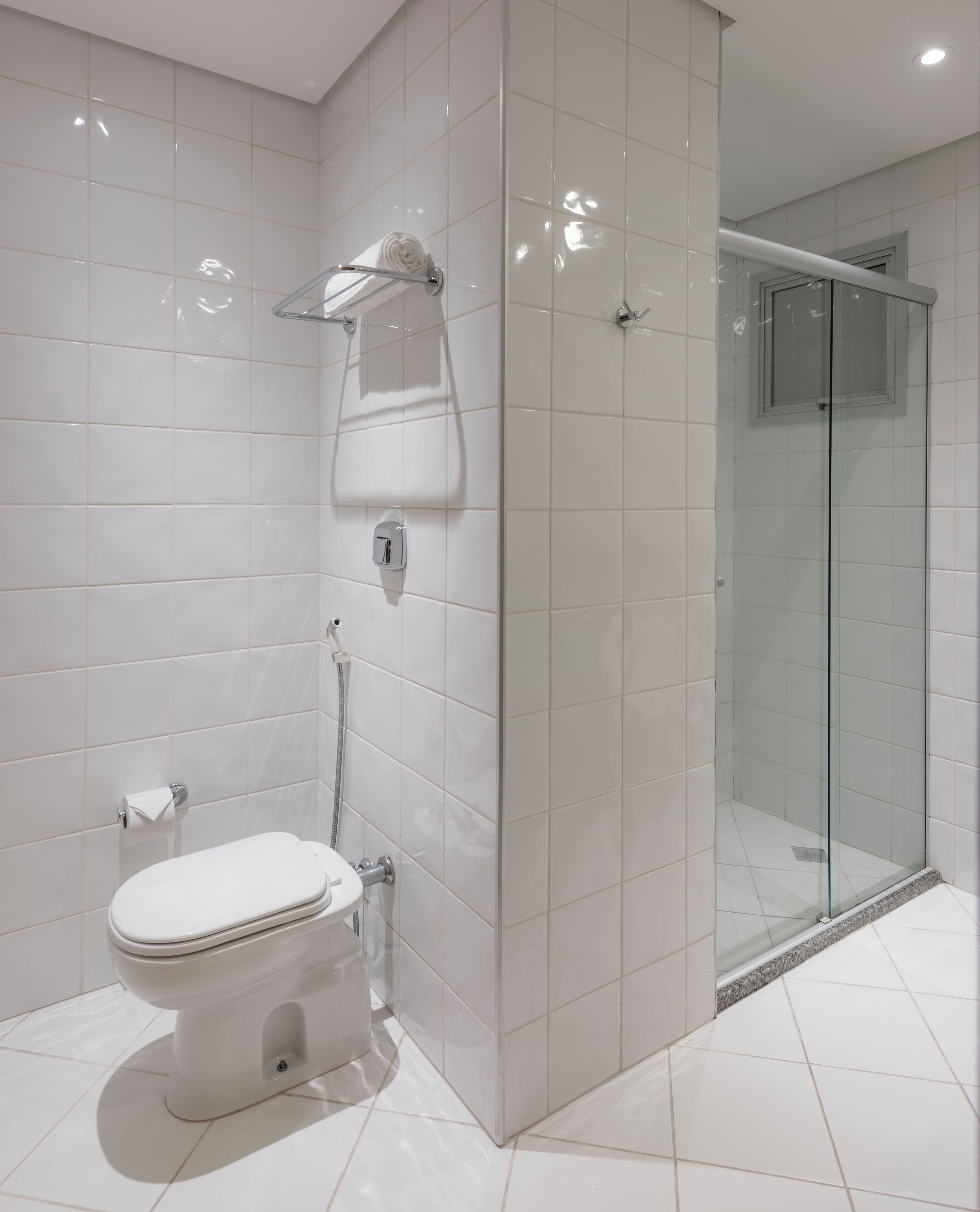 Un baño moderno con azulejos blancos, inodoro, cabina de ducha de vidrio y un perchero para toallas.