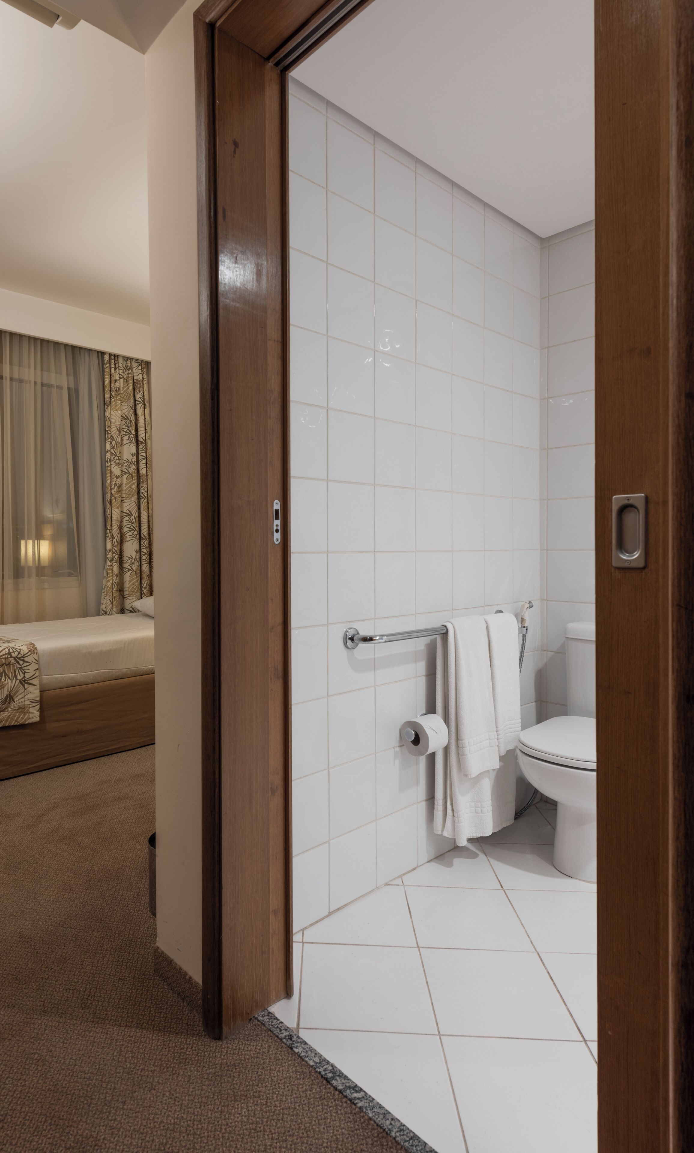 A modern bathroom with white tiles, a toilet, a shower, and a towel rack.