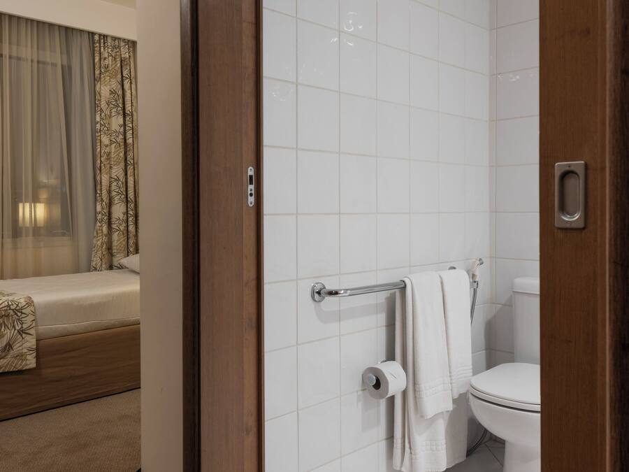 A modern bathroom with white tiles, a toilet, a shower, and a towel rack.