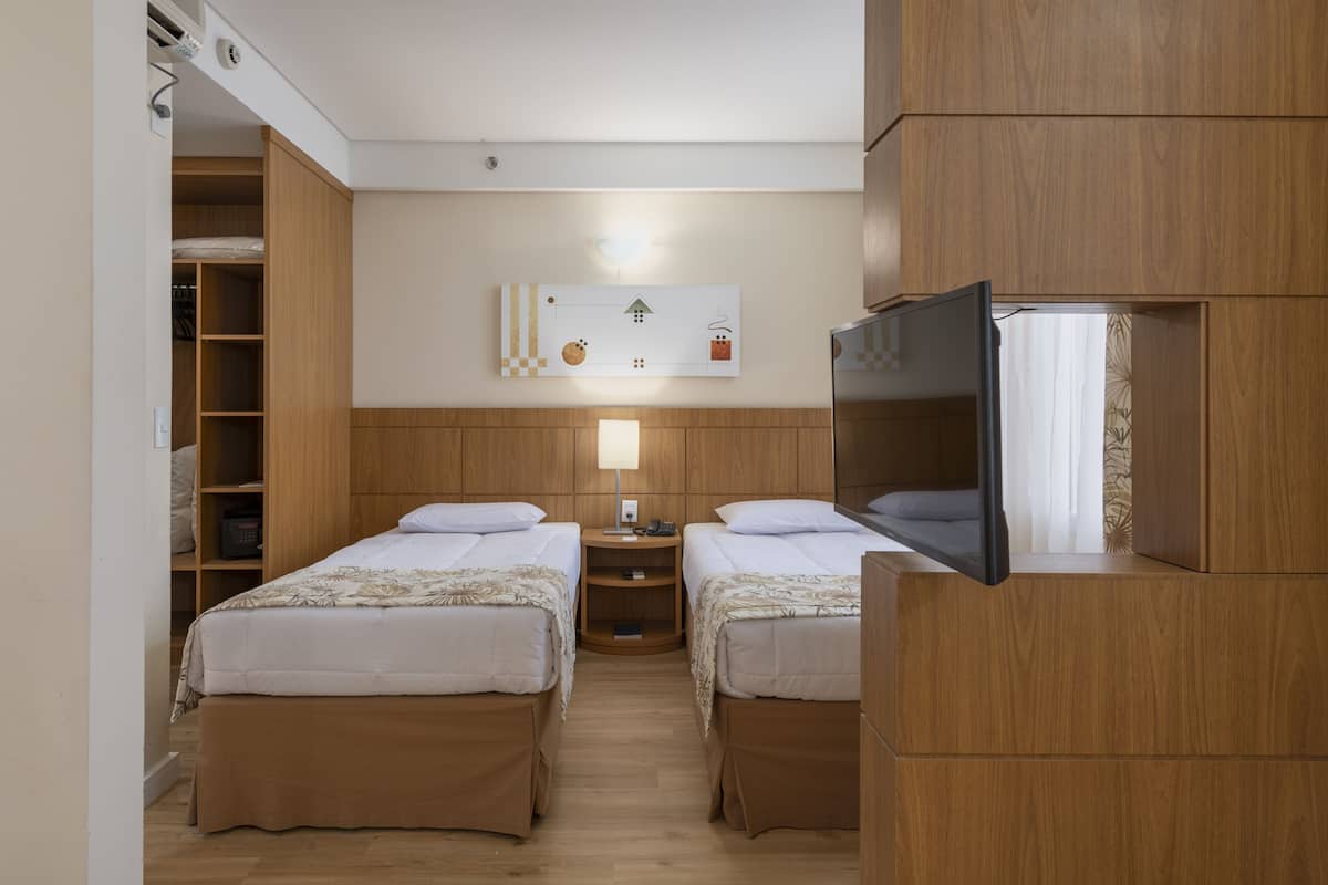 A hotel room with two beds, a TV, a bedside table, a lamp, and a wardrobe.