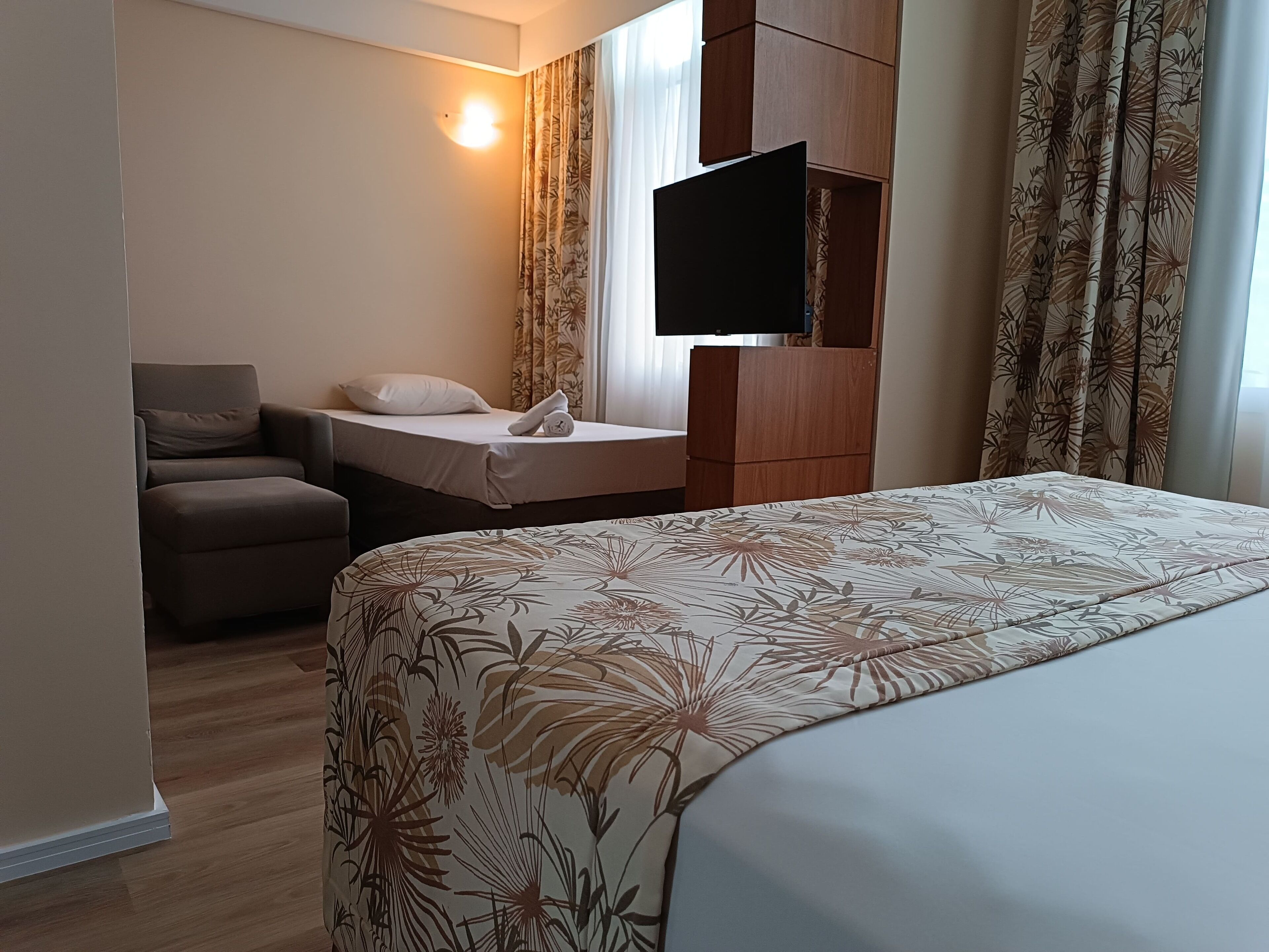 A hotel room with a bed, a desk, a chair, a flat-screen TV, and a wardrobe.