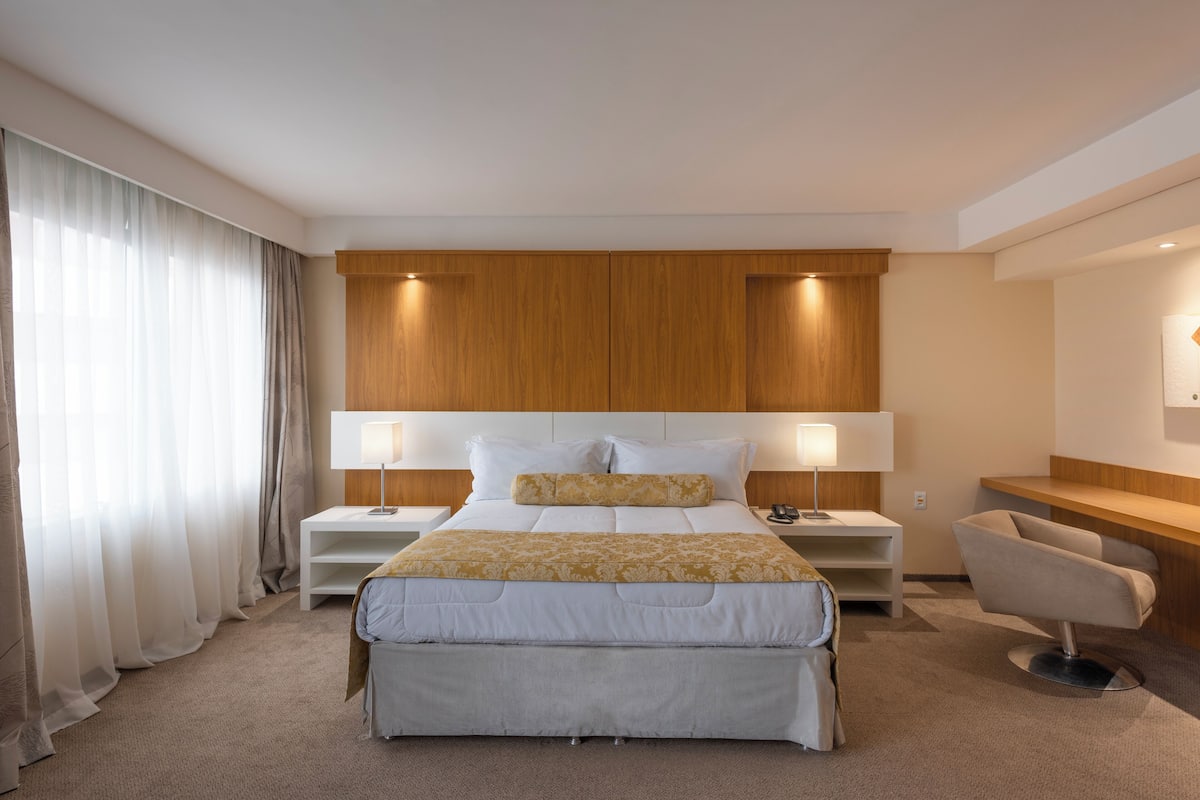 A modern hotel room with a large bed, two bedside tables, a desk, and a chair.
