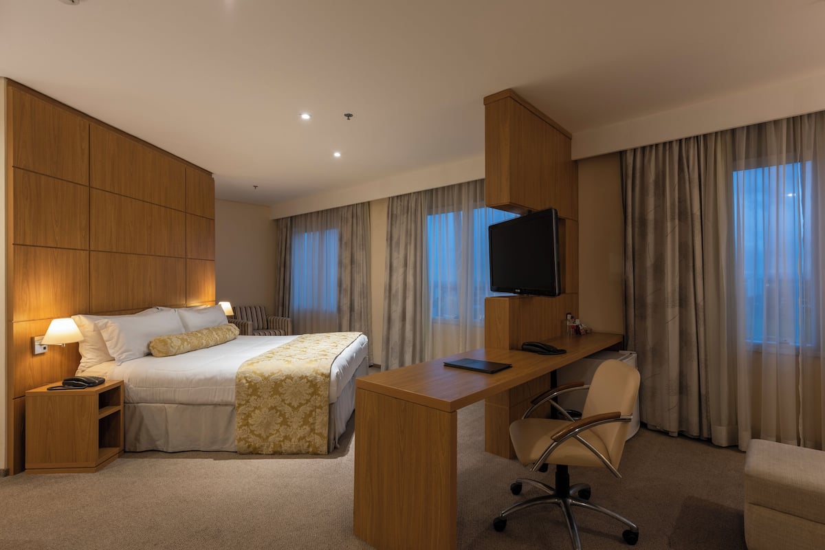 A hotel room with a bed, desk, chair, television, and curtains.