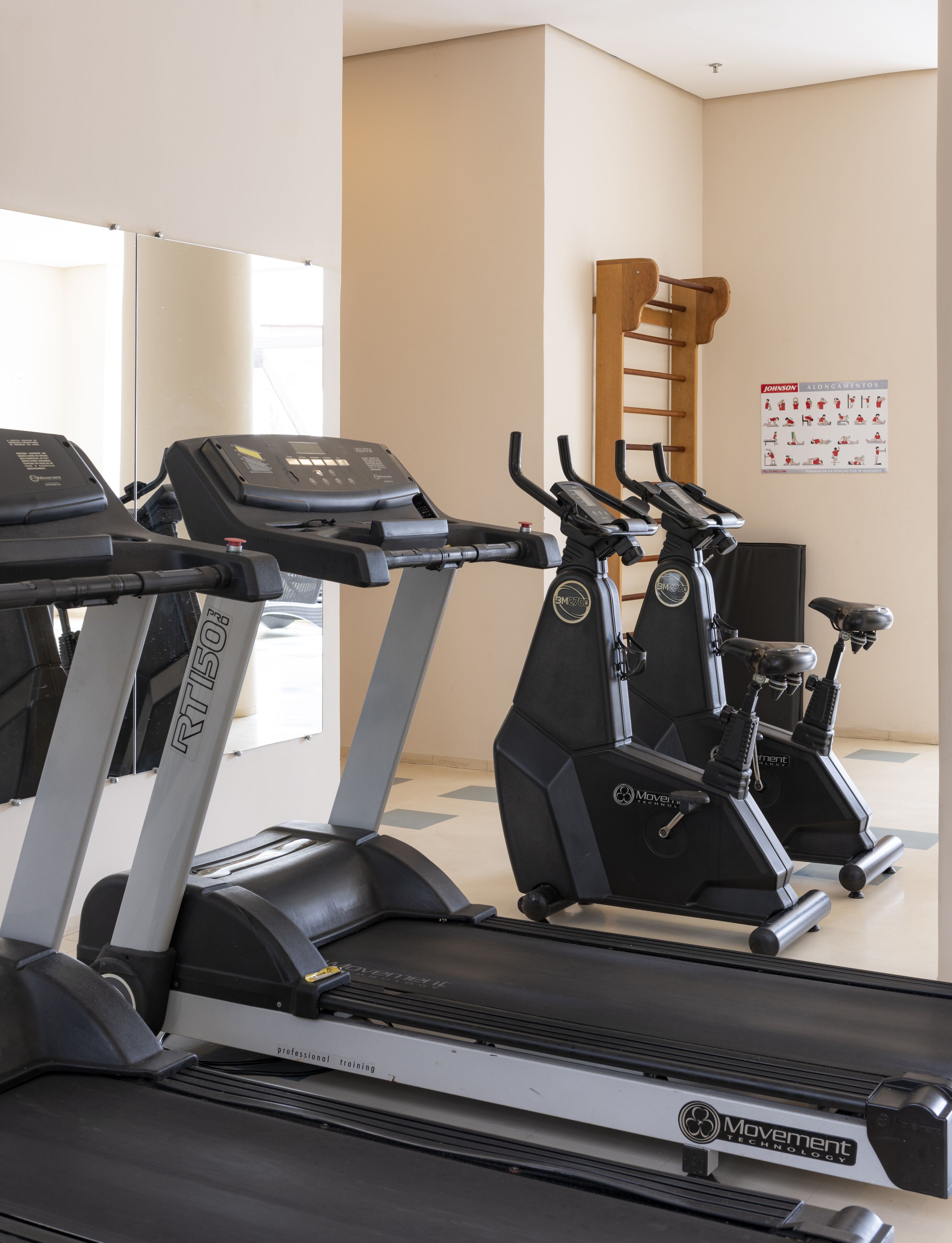 A gym with treadmills and stationary bikes, a wooden chair, and a poster on the wall.