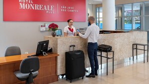 Un mostrador de recepción de hotel con un cartel rojo, una recepcionista y un huésped con una maleta.