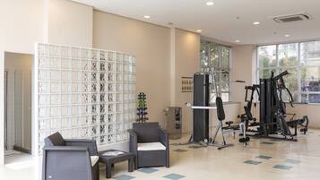 Un gimnasio espacioso con equipo de ejercicio, una pared con azulejos decorativos y zonas de descanso.