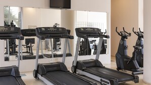 Un gimnasio con cintas de correr, elípticas y un televisor montado en la pared.