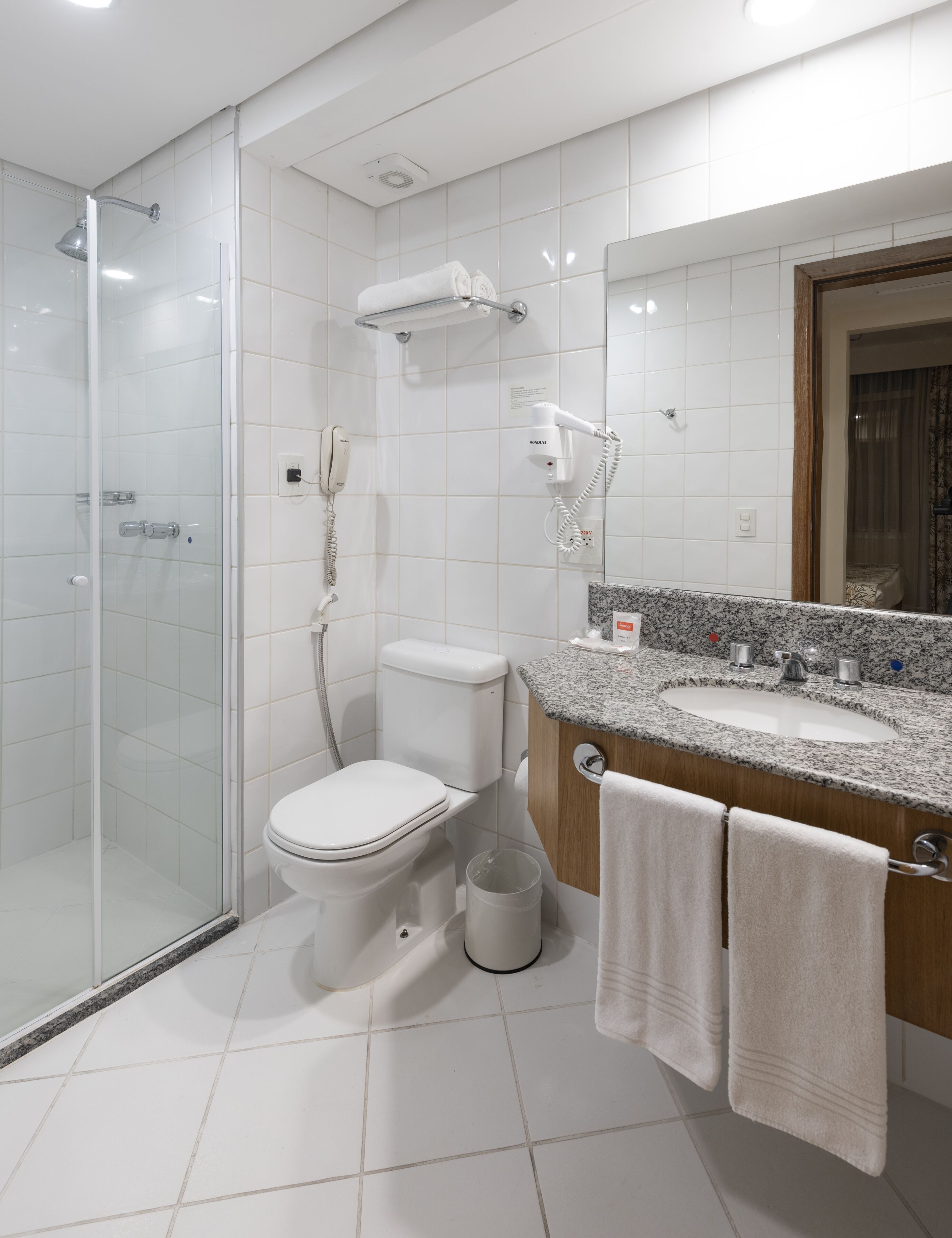 Une salle de bain moderne avec une douche à parois de verre, des toilettes, un lavabo avec un plan de travail en granit et un miroir.