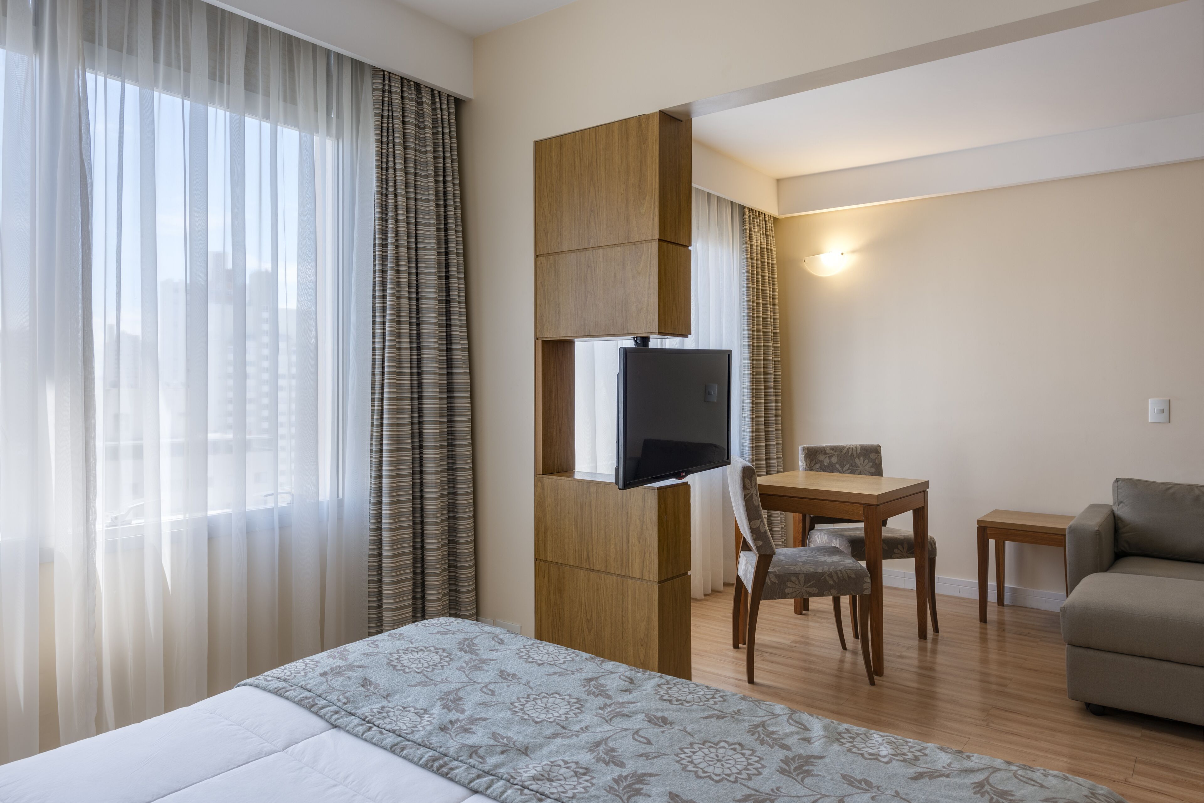Une chambre d’hôtel comprenant un lit, un téléviseur fixé sur un panneau en bois, une table à manger avec des chaises et un canapé.
