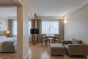 Una camera d'albergo con un letto, una TV, un tavolo da pranzo con sedie, un divano e un armadio in legno.