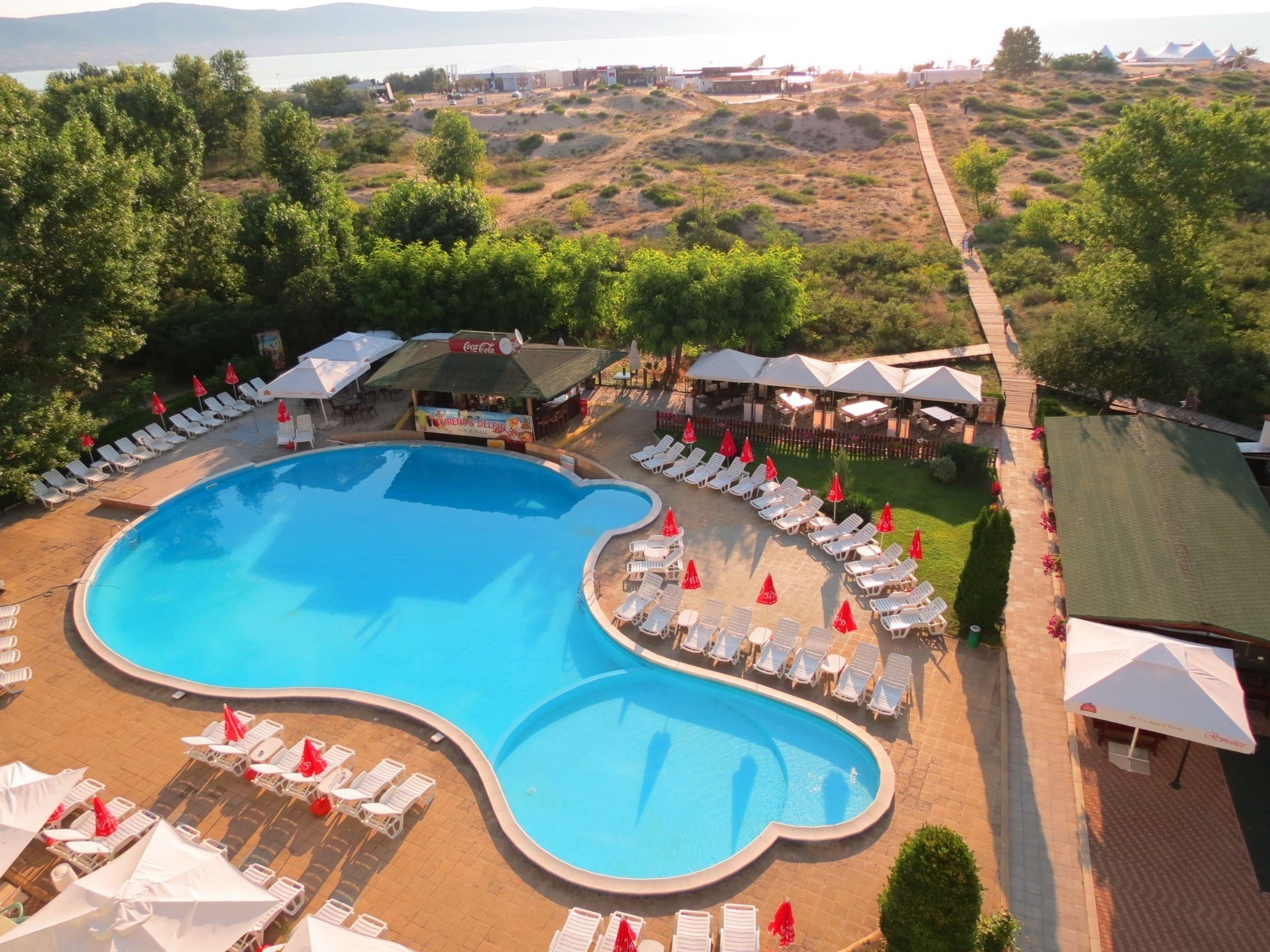 Una piscina amplia con tumbonas y sombrillas, rodeada de vegetación y vistas al mar.