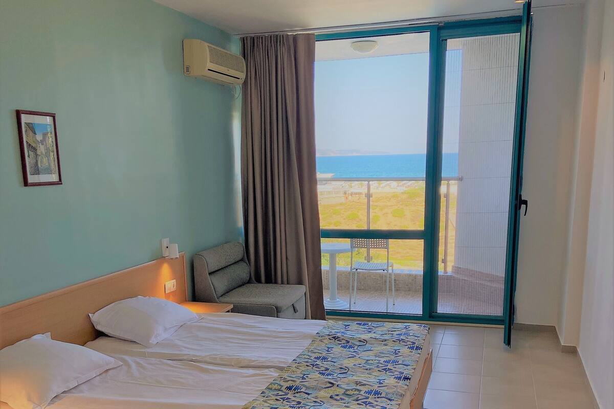 Une chambre d’hôtel avec un lit, un bureau, une chaise et un balcon donnant sur la plage.