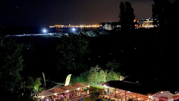 A nighttime view of a resort with a large swimming pool, outdoor seating areas, and a view of the city skyline. - Sirena Hotel (Sunny Beach)