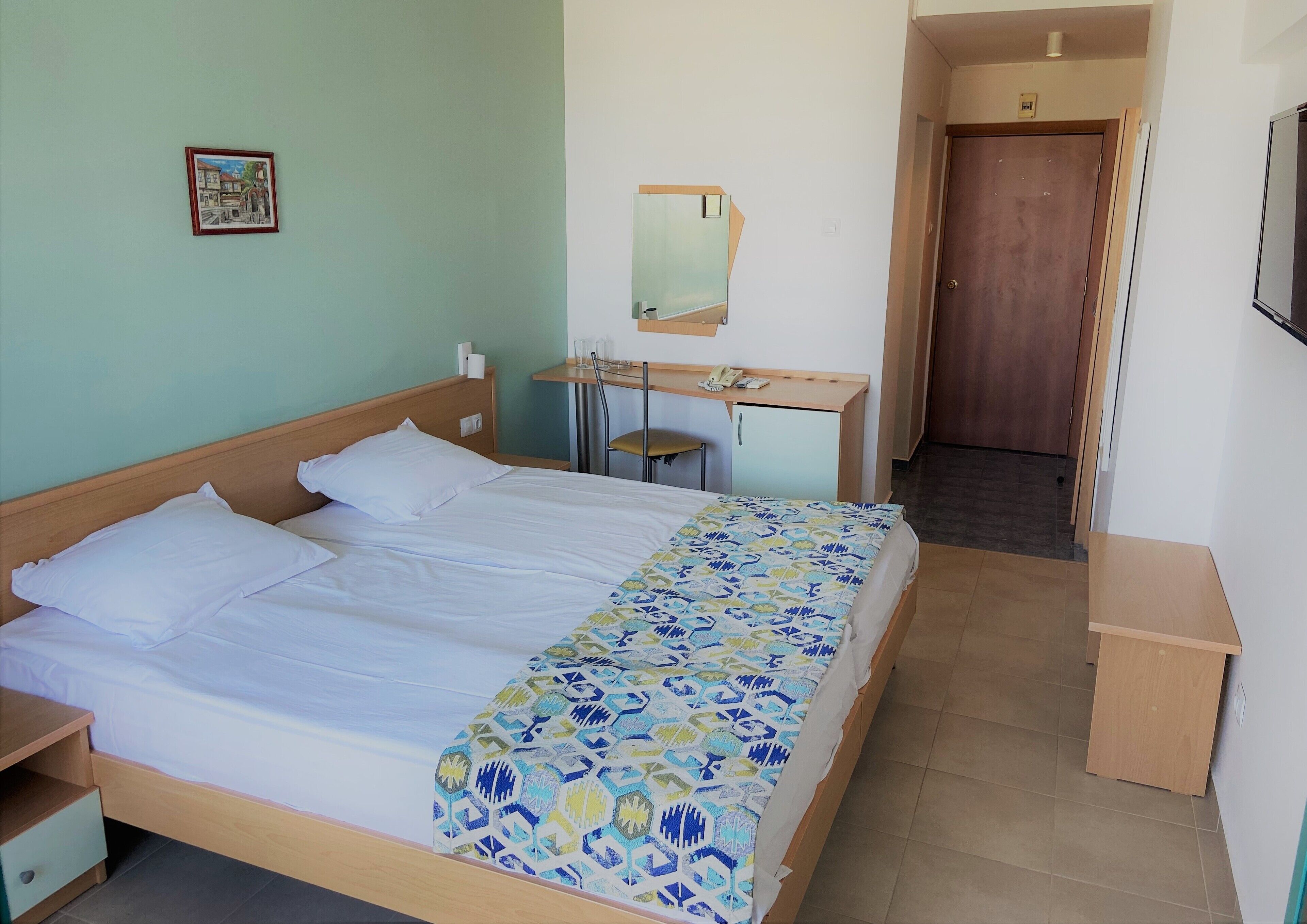 Een hotelkamer met een bed, een bureau, een stoel, een spiegel en een deur.