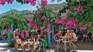 Un espace extérieur aménagé avec des tables et des chaises, entouré d’une végétation luxuriante et de fleurs roses.