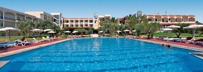 Una piscina con sillas de descanso y sombrillas, rodeada de edificios de hotel con varios balcones.