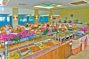 A buffet setup with multiple food stations, tables, and chairs arranged in a spacious room. - Marianna Palace (Rhodes)