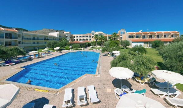 A swimming pool surrounded by sun loungers and umbrellas, with a building in the background. - Marianna Palace (Rhodes)