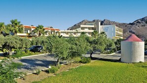 A hotel with multiple buildings, palm trees, and a mountainous backdrop. - Marianna Palace (Rhodes)