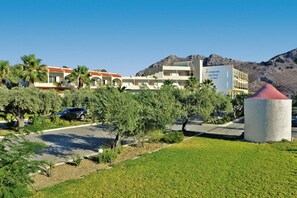 A hotel with multiple buildings, palm trees, and a mountainous backdrop. - Marianna Palace (Rhodes)