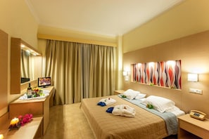 A hotel room with a bed, a desk with a mirror, a telephone, and a wall-mounted TV. - Marianna Palace (Rhodes)